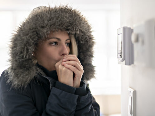 Homeowner in parka looking at thermostat