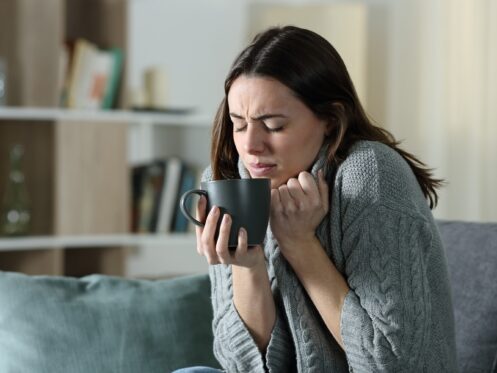 Woman getting cold holding coffee mug at home
